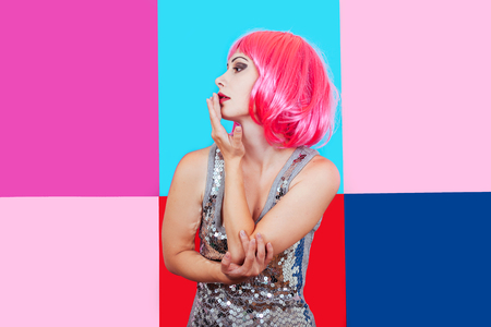 Beautiful girl with pink hair dressed in silver dress on a multicolored graphic background. Gently woman touches face her hands and dreams.の写真素材