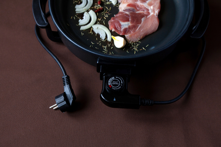 Electric pan with meat on the table. Independent auxiliary skillet for cooking any place.の写真素材