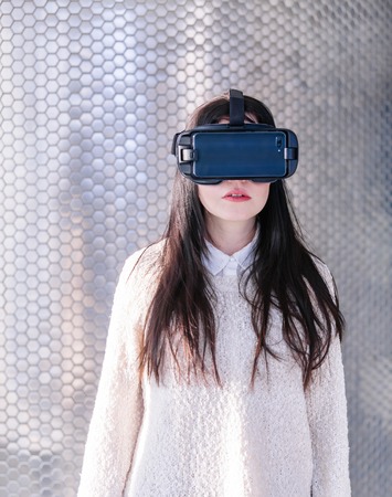 A young girl with a headset on the face meets new technologies. Woman using virtual reality headset.の写真素材