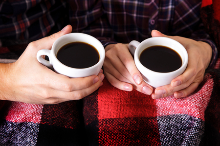 Young couple's hands with two cups of hot coffee. Man and woman together in a warm blanket.の写真素材