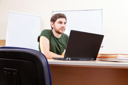 Portrait of informal male teacher in classroom on lesson. Creative young man teaches online on the computer.の写真素材