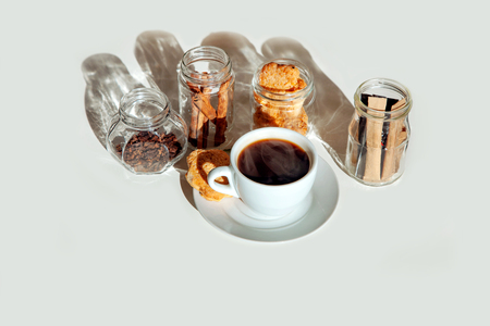 Sticks of sugar and spices in transparent jars with a cup of tea with milk. Cup of coffee and cinnamon into glass jars on white background.の写真素材