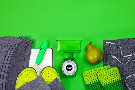 Fitness and healthy active lifestyle, sport shoes, scales, sneakers headphones, hat and clothes for sport with pear on the green background.の写真素材
