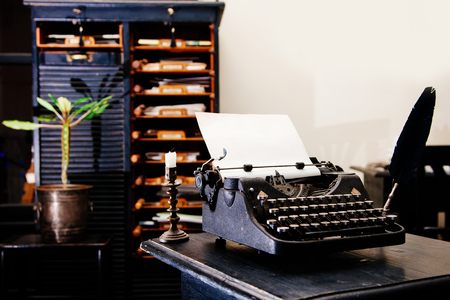 Old antique manual typewriter on the table of the writer in front of the old cupboard with papers.の写真素材