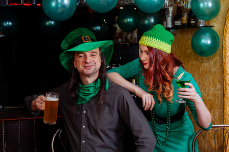 The company of young girls and one man celebrate St. Patrick's Day. They have fun at the bar. They are dressed in carnival headgear, green hats and clothes.の写真素材