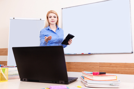 Portrait of blonde female teacher in classroom against the white school board.の写真素材