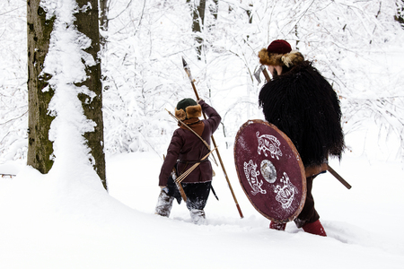 Father and son Vikings in a deep winter forest and the father teaches his son to be a real Viking. Viking warrior with chain mail leather spear walking in winter woods before battle, scandinavian traditional clothing for lumberjack, viking concept.の写真素材