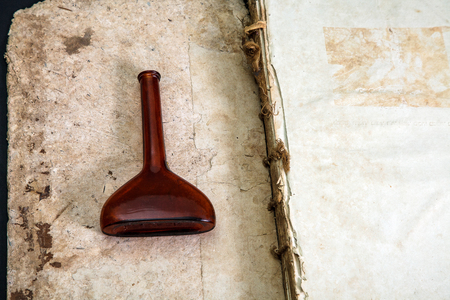Old book cover, vintage texture, isolated on black background. On an open old book lie an old brown pharmacy flask or a vessel.の写真素材