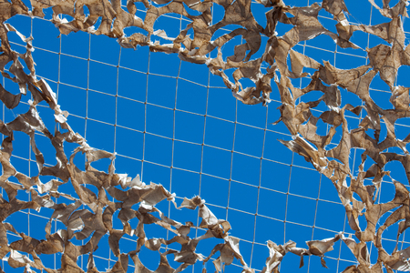 White military mesh with torn holes with shadows from bright sunlight. Camouflage net and the blue sky.の写真素材