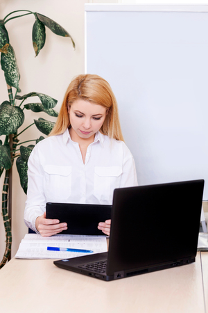 Portrait of blonde young woman on the white mackground. Girl dressed in white shirt warks at the computer online.の写真素材