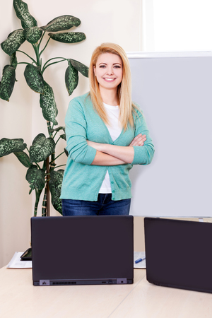 Portrait of blonde young woman on the white background. The teacher or manager stands near the school board.の写真素材