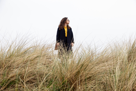 A lonely girl with long curly hair against of the sky against the dried grass. Portrait of a woman on sea, wind, rain.の写真素材