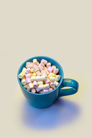 Blue cup of coffee on the white table. A cup of chocolate sprinkled on top with a little white and a pink marshmallow.の写真素材