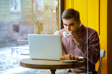 Man use laptop connecting wifi internet, businessman busy at office desk, finger typing on computer sitting at wooden table in cafe with cup of coffee and with croissant.の写真素材