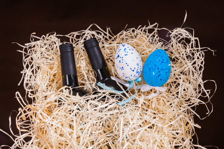 Two bottles of red vine and two white and blue eggs in box with straw. Easter concepts with gifts on yellow straw background.の写真素材