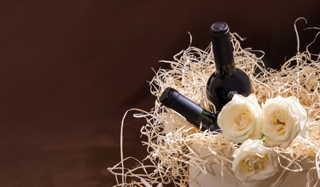 Two bottles red vine and white roses in box with straw. Holiday concepts with gifts and roses on yellow straw background.の写真素材