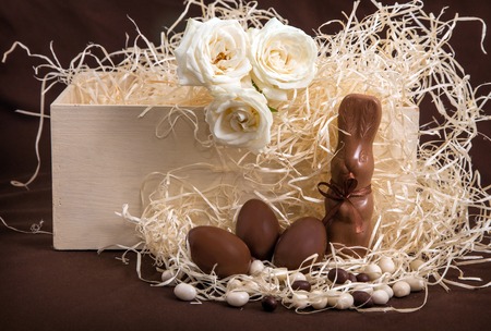 Chocolate bunny and three eggs in box with straw. Easter traditional celebtation in Netherlands with gifts and roses on yellow straw background.の写真素材