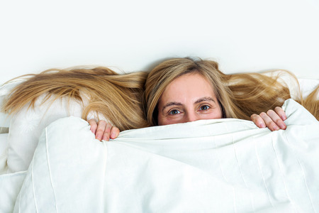 Beautiful middle aged fifty plus woman lies a covered blanket, smiling and looking at the camera. Real portrait with wrinkles of a happy woman during menopause.の写真素材
