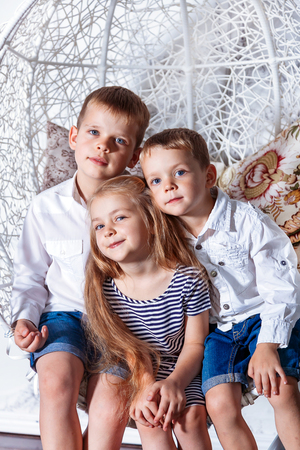 Two brothers and a sister with blue eyes looking at the camera together. Group of happy smiling kids sitting together.の写真素材