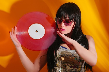 Young DJ woman with pink vinyl enjoys music. Glamorous hippie brunette on hot yellow background with sunlight and shadow.の写真素材