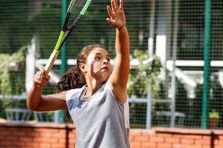 Girl teenager with long curly hair with a racket in his hands. Girl tennis player on the court in summer.の写真素材