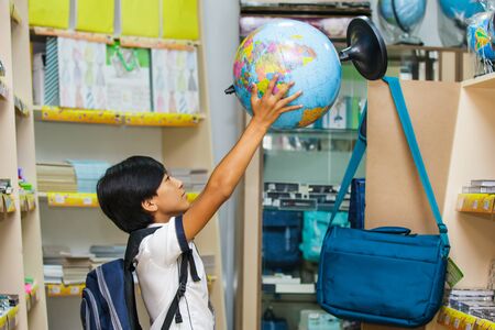 Asian boy chooses stationery in the submarket. The schoolboy holding a globe and buying.の写真素材
