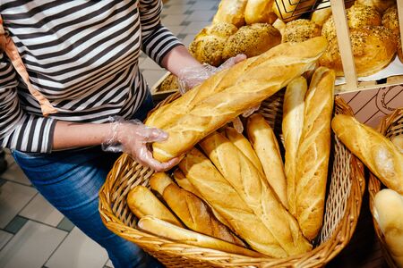 Female hands takes bread from wicker basket in the bakery. Fresh baguette in supermarket or batch.の写真素材