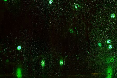 Rain drops on window with bokeh on blure background. Night on the street and a lot of multicolored lanterns behind wet glazing.の写真素材