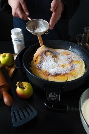 Traditional Dutch Pancakes with apples on the electric iron pan on the black background.の写真素材