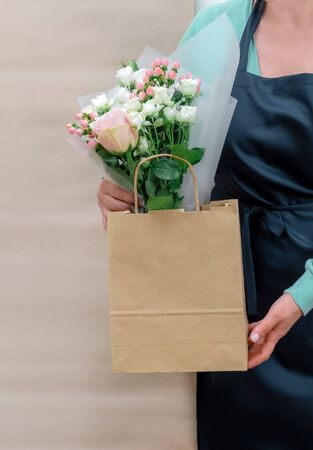 Female Worker of Delivery Service in Uniform Packing Flowers in paper bag for Customer on the White and Craft Background.の写真素材