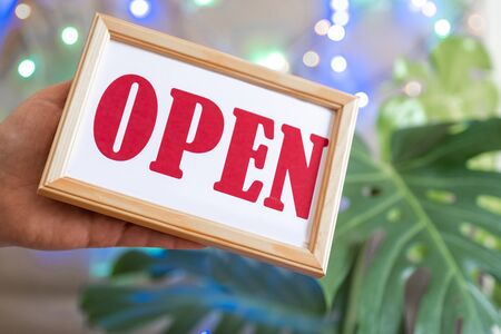 Woman's hands holds dashboard with text open. Worker in apron shows through lights of showcase opening of the cafe or market.の写真素材