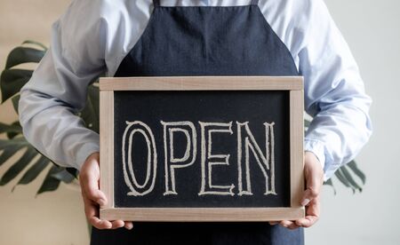 Woman's Hands Holds Dashboard with Text Open. Worker in apron Shows Opening of the Cafe or Market.の写真素材