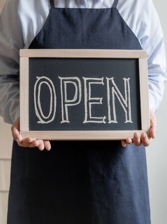 Woman's Hands Holds Dashboard with Text Open. Worker in apron Shows Opening of the Cafe or Market.の写真素材