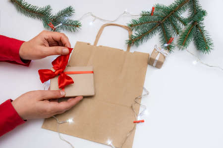 Hands hold gift's box on a festive background with bag, boxes and christmas treeの写真素材