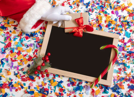 Hand of Santa Claus holds gift on the bright confetti background with shopping board.の写真素材