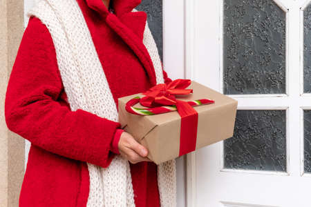 Deliver dressed in red coat holding Gift's Boxes near the white door on the eve of holidays Christmas and New Year.の写真素材
