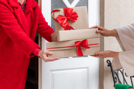 Worker dressed in red coat delivering Gift's Boxes near the white door on the eve of holidays Christmas and New Year.の写真素材