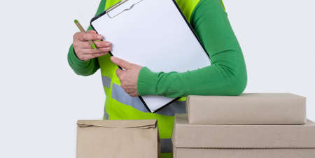 Female worker is in a green vest standing near a lot of paper boxes with blank order, delivery concept.の写真素材