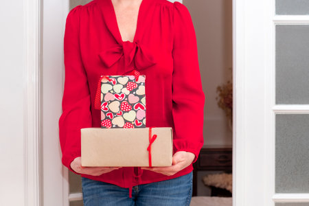 Woman's hands holding Shopping bag with red Hearts of Valentine's Day and Gifts Boxes near the white door.の写真素材