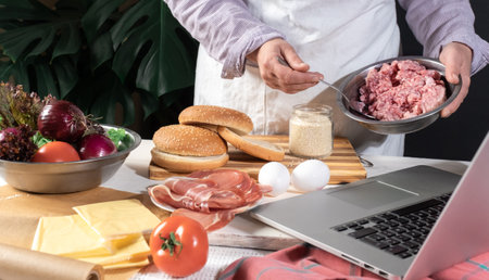 Female Chef cooking Big Burger or Cheeseburger and Using Laptop with Cooking Recipe Tutorial.の写真素材