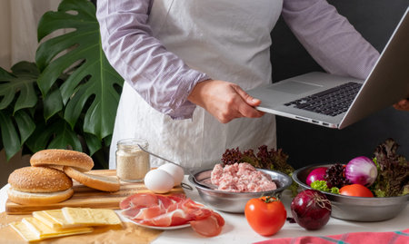 Female Chef cooking Big Burger or Cheeseburger and Using Laptop with Cooking Recipe Tutorial.の写真素材