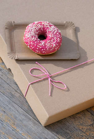Pink Cake on the paper delivery box with red bow on the wooden background, top view.の写真素材
