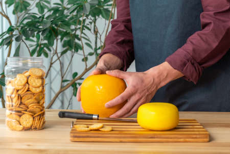 Hands of man hold whole holland cheese Edam and dutch goat cheese from Netherlands on the kitchenの写真素材