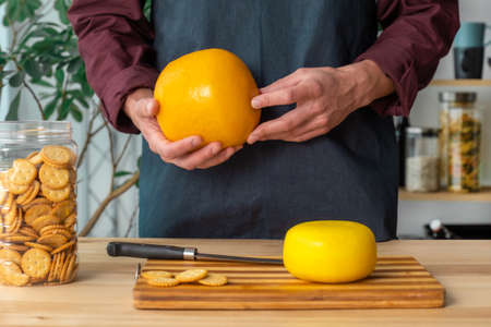 Hands of man hold whole holland cheese Edam and dutch goat cheese from Netherlands on the kitchenの写真素材