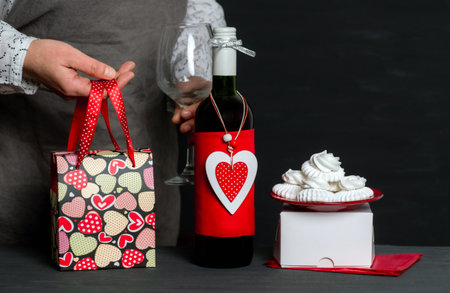 Deliver Holding Wineglass near Wine Bottle with red Heart of Valentine's Day, festive bag and cakesの写真素材