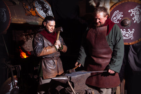 Viking forges weapons and swords in the smithy. A man in a warrior's clothes is in the smithy on the background of fire.の写真素材