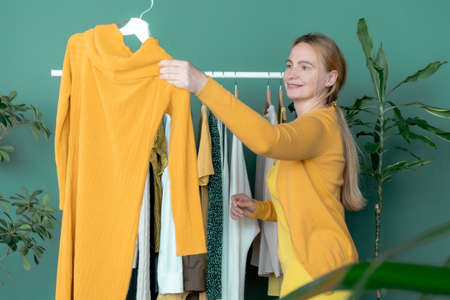 Middle Aged Blond Woman makes shopping and looks at the new yellow dress near shelf with clothesの写真素材