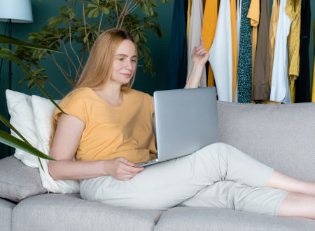 Middle Aged Blond Woman sitting on the sofa and communicates online by Laptop.の写真素材