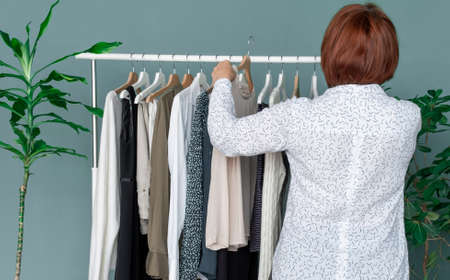 Middle Aged Woman makes shopping and looks at the new dress near shelf with clothes.の写真素材