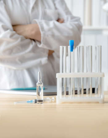 Doctor stands near table with test tubes, ampoule and syringe, concept of global vaccination.の写真素材